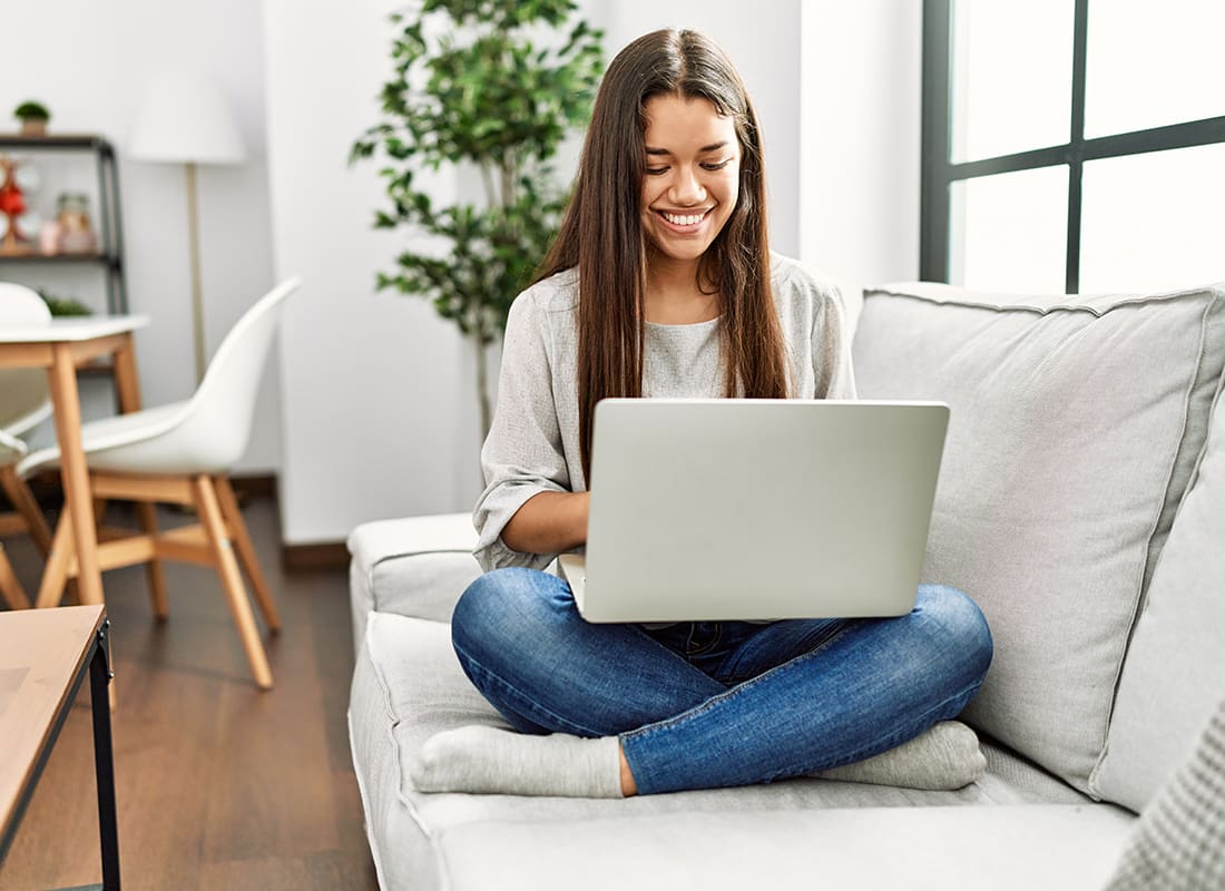 Service Center - Young Woman Sitting on Her Sofa Reading on Her Laptop